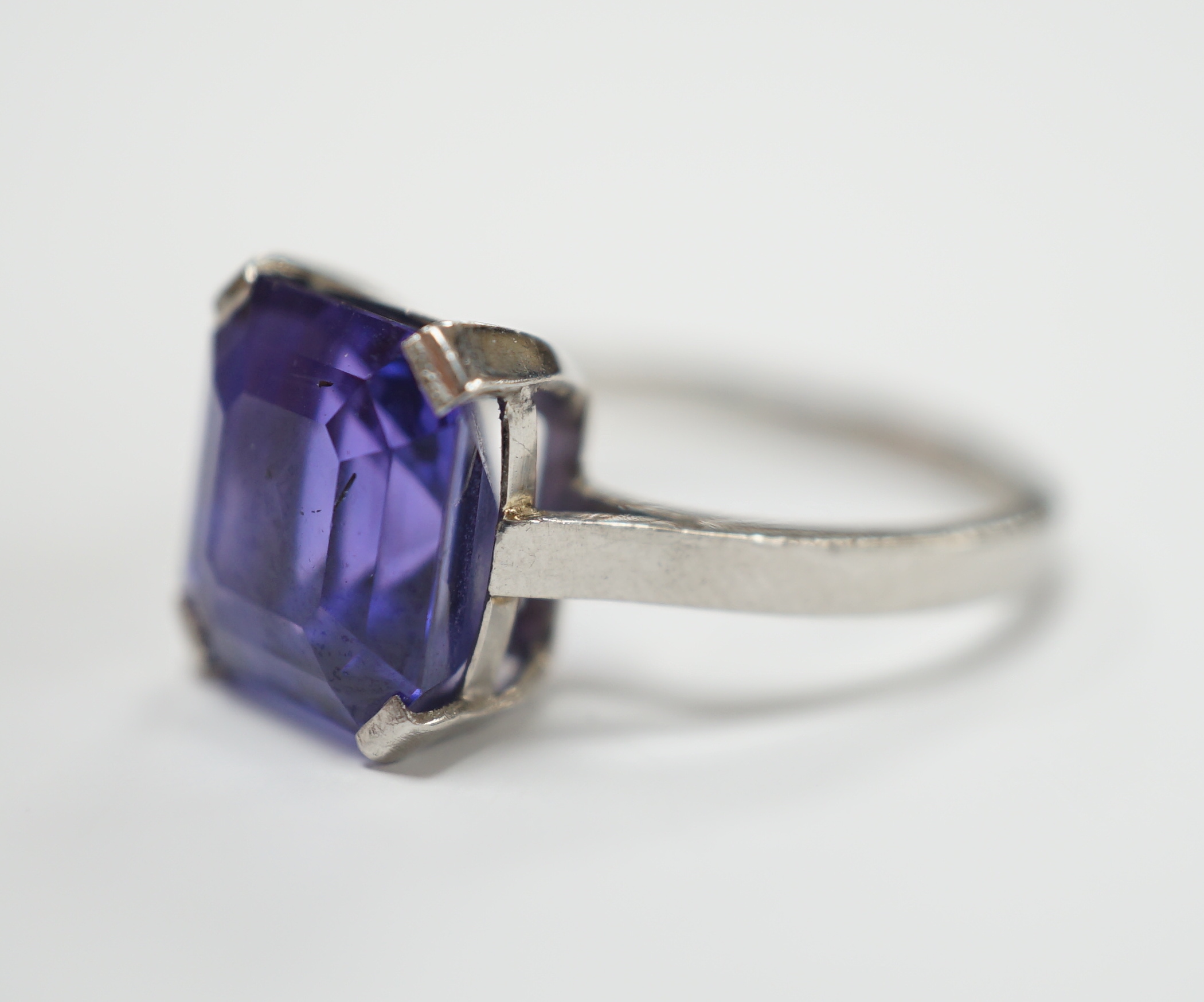 A white metal and single stone and square cut blueish purple sapphire set dress ring, size M, gross weight 5.6 grams, the stone measuring 10mm by 9,8mm, with a depth of 7.4mm.